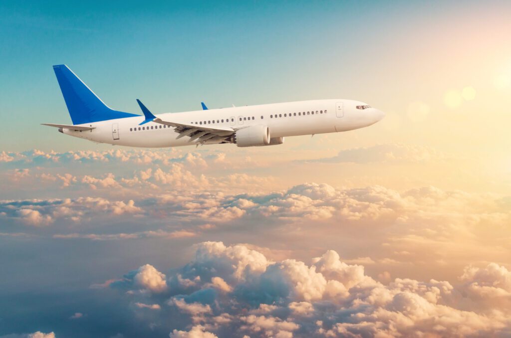 Commercial airplane flying above cloudscape in dramatic toned sunset light.